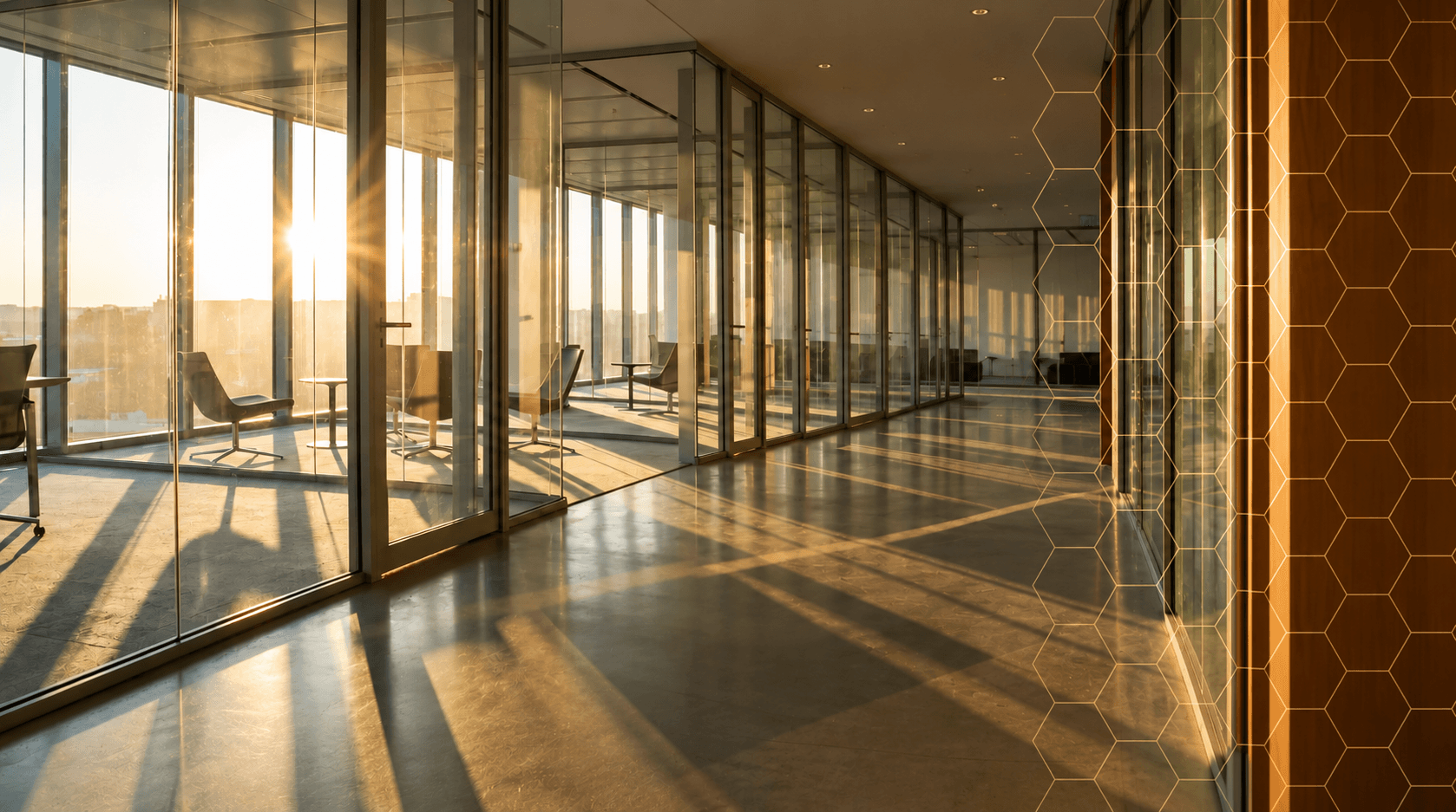 Modern glass office hallway illuminated by golden sunset light with long, dramatic shadows.
