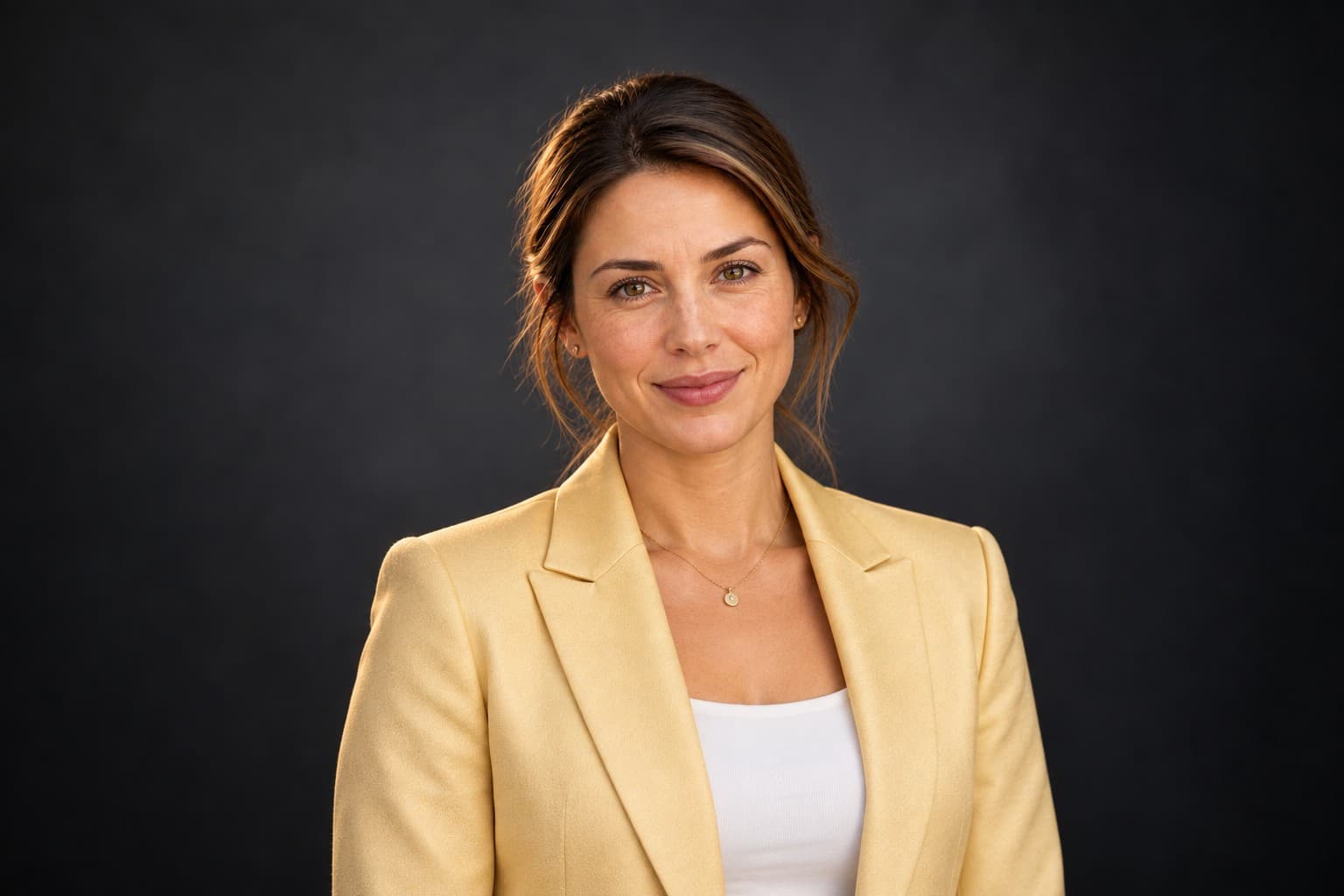 Smiling woman with brown hair in a yellow blazer against a dark textured background.